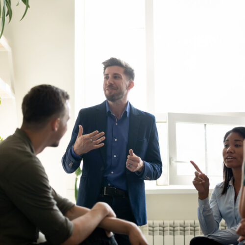 Group of diverse corporate office members chatting during break gathered together in co-working space, discussing new project, share thoughts, enjoy informal friendly talk, communicating solving issue